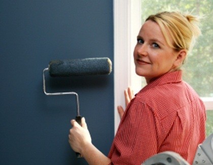 woman painting blue wall with roller brush