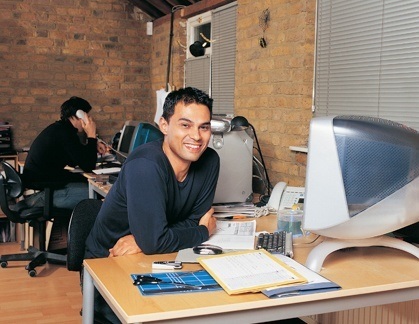 Smiling industrial designer working at a computer with plans